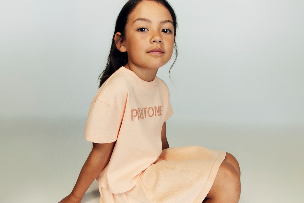 A young girl sat down wearing a pink top with Pantone on the front and a matching pink skirt 