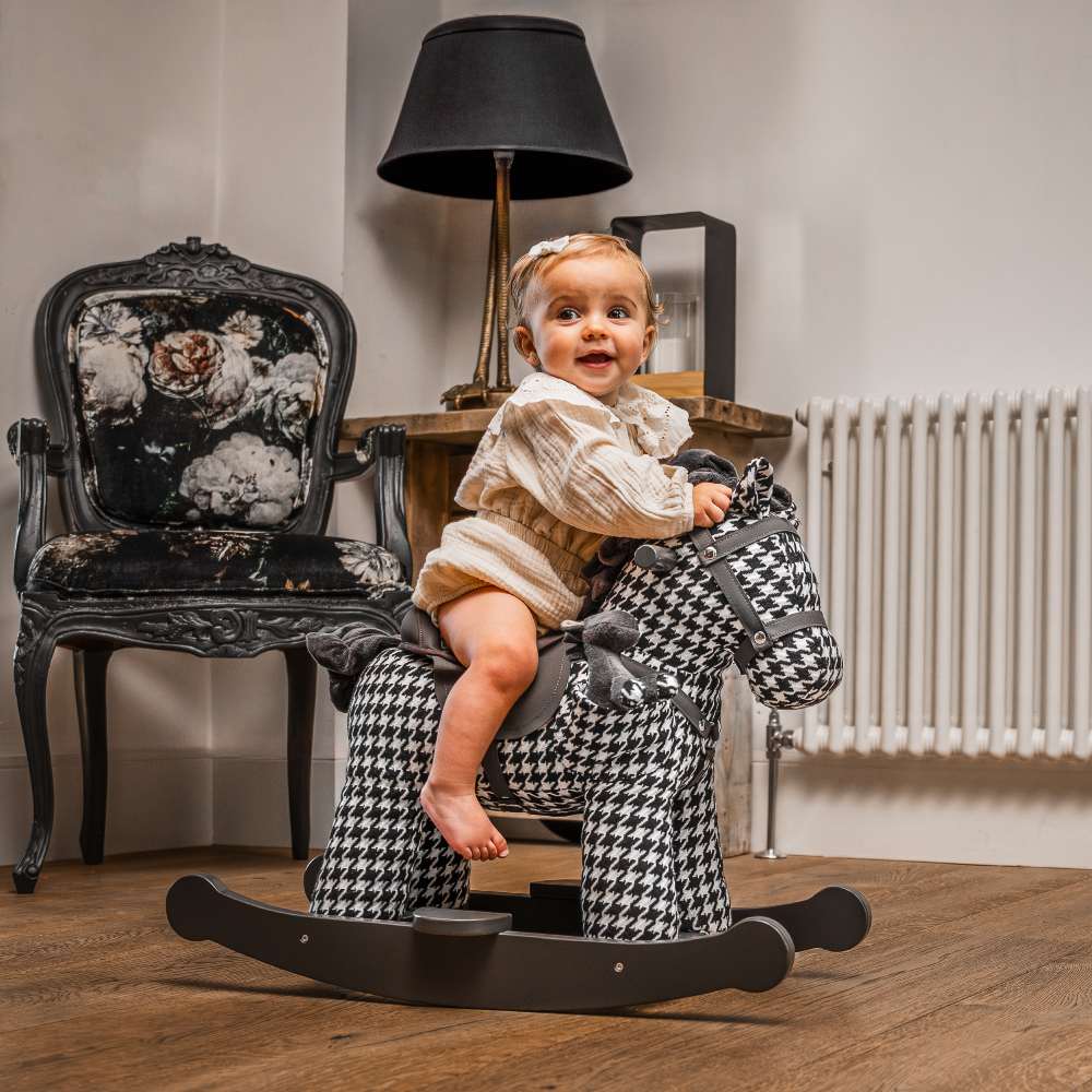 A young child sat on a black and white houndstooth print rocking horse 