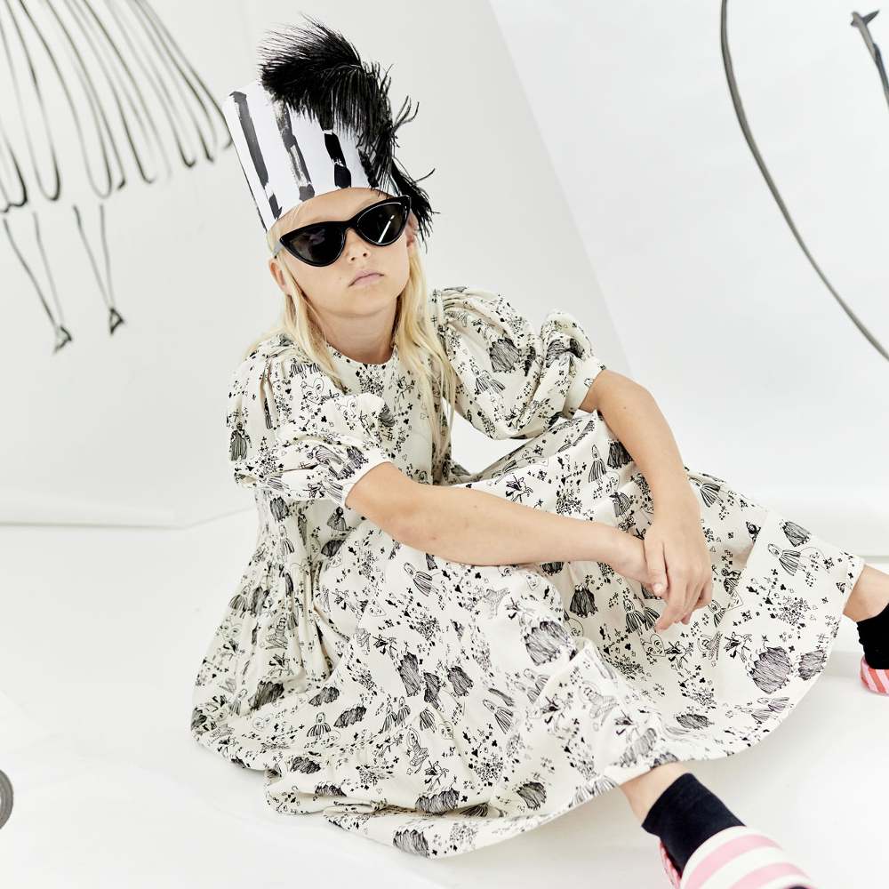 A girl sat on the floor wearing black sunglasses and a black and white print dress 