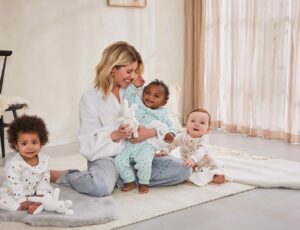 Mollie King sat on the floor with three babies wearing the new Maybe Baby clothing range by Boots