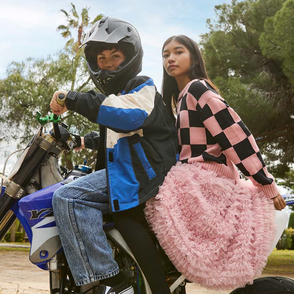 A young boy on a motorbike in a helmet with a girl sat behind in a pink and black cardigan and pink skirt 