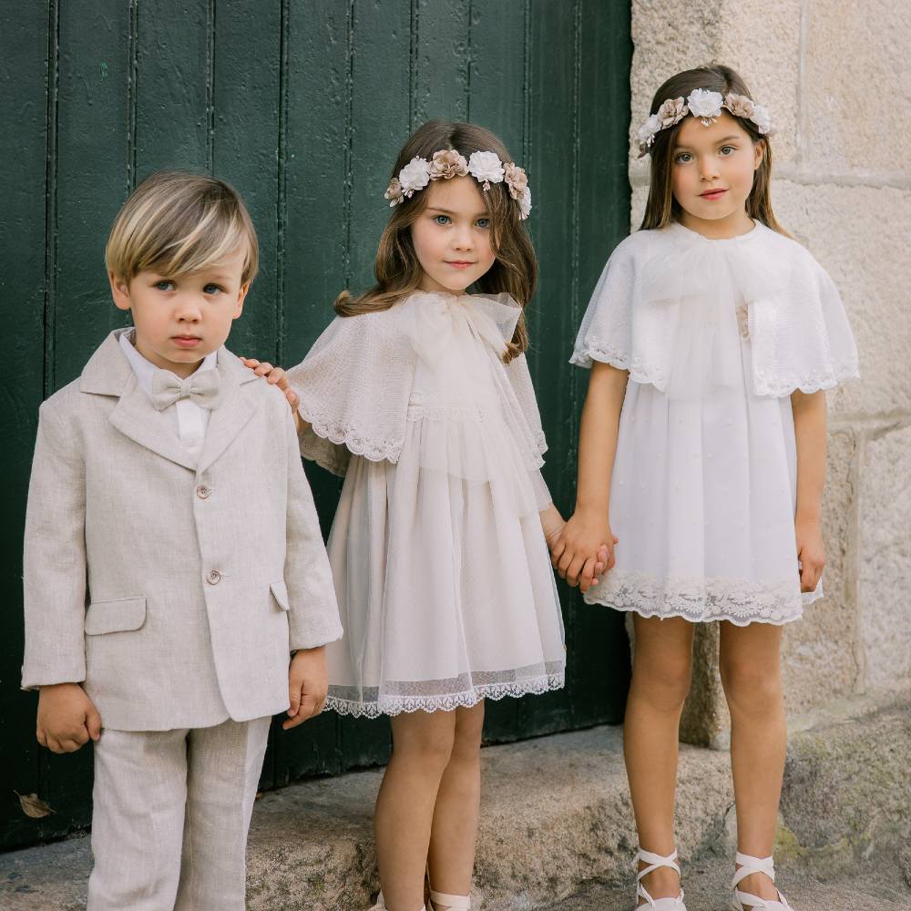 Three children stood outside in front of a green door wearing special occasionwear