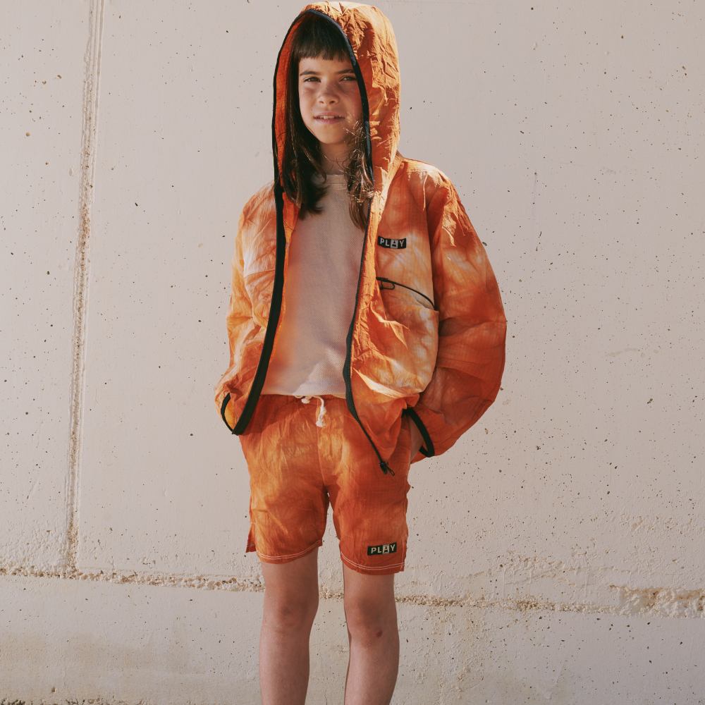 A young child stood in an orange hooded top and shorts 