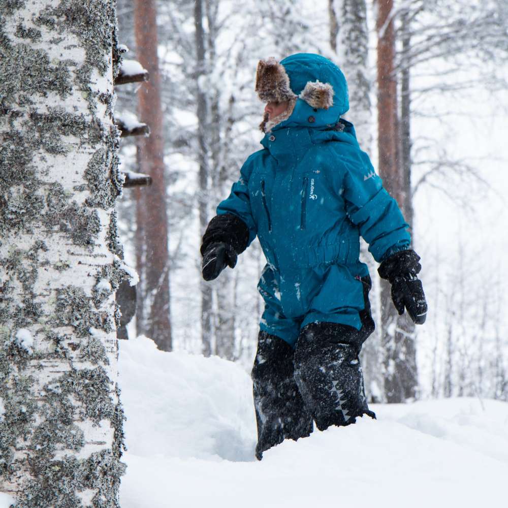 A child in a blue coat stood in a wood in snow 