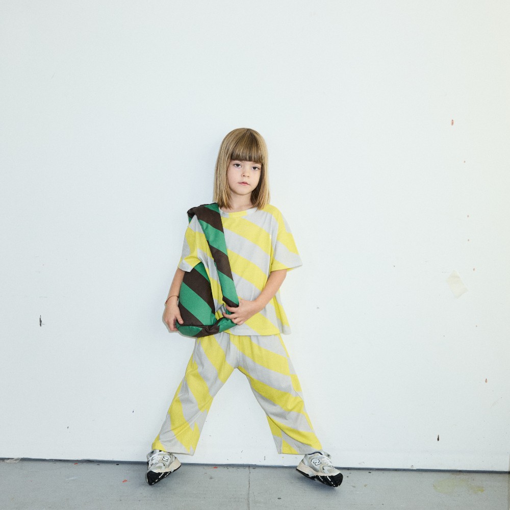 A young girl in a yellow and grey striped top and trousers holding a green and black striped bag