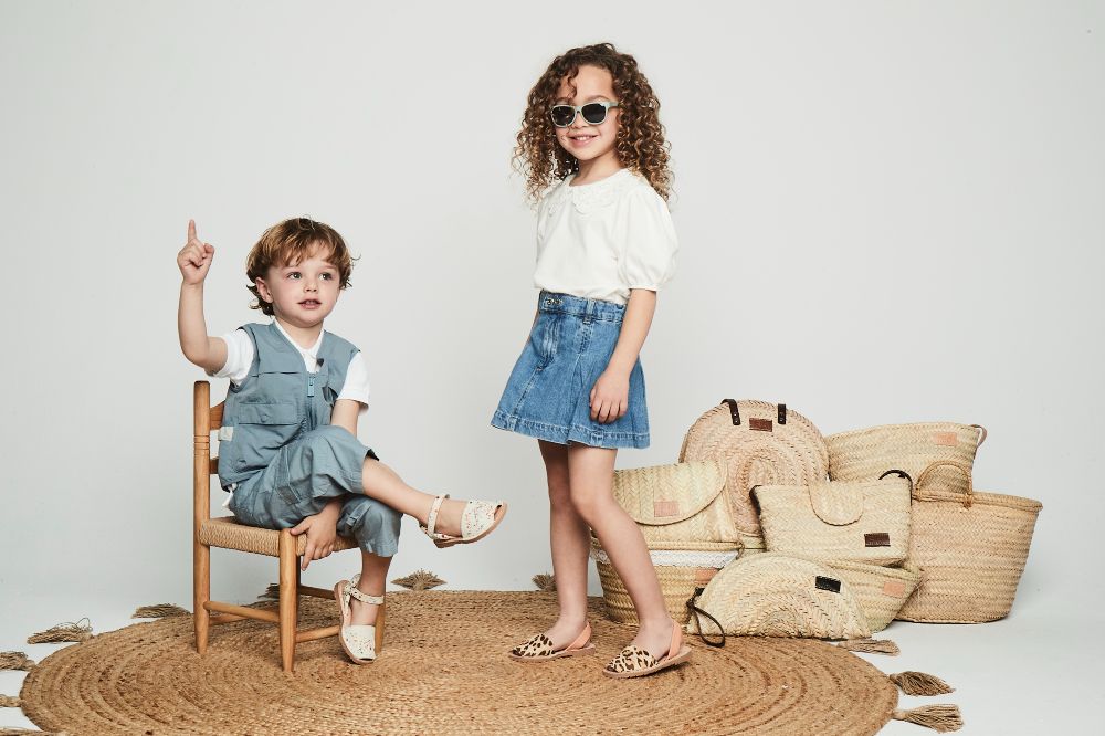 A young boy sat on a chair beside a girl and a pile of bags 