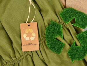 A green garment with a 100% recycled fabric tag on it and a recycle symbol