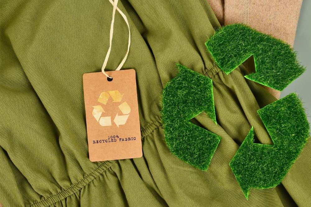 A green garment with a 100% recycled fabric tag on it and a recycle symbol