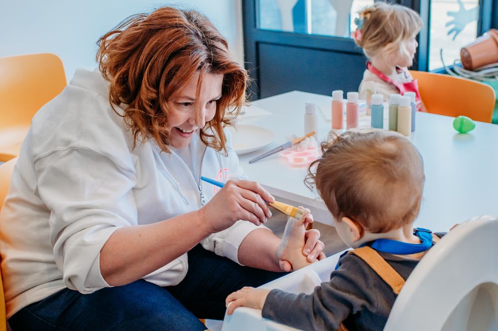 A woman feeding a baby in a highchair in a nursery