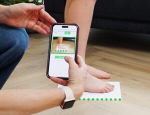 A person knelt down measuring a child's foot with the Sizewise digital measuring tool