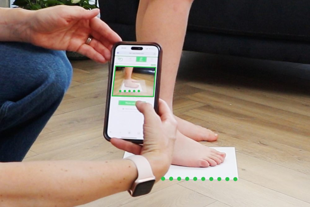 A person knelt down measuring a child's foot with the Sizewise digital measuring tool