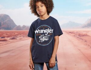 A boy in a Wrangler® T-shirt and jeans stood against a background of a desert road