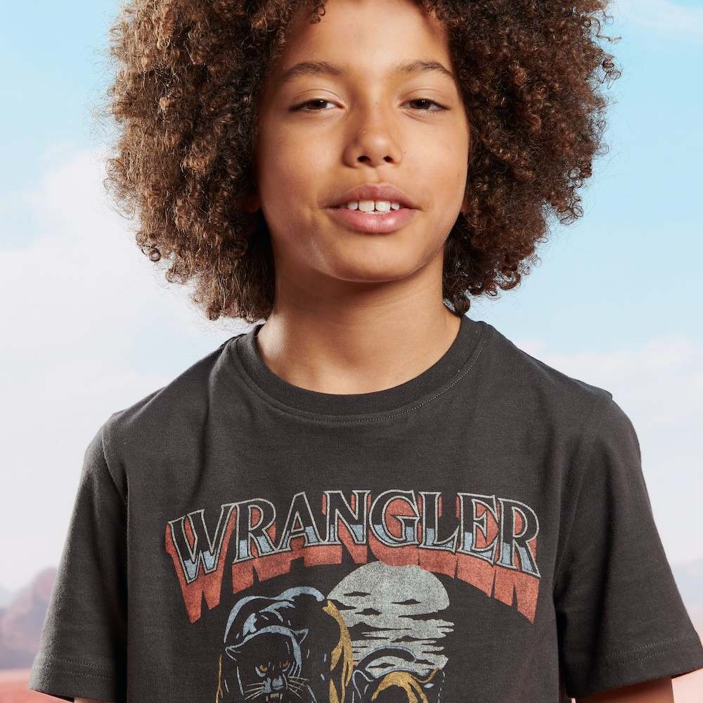 A boy wearing a black T-shirt with the Wrangler logo on the front