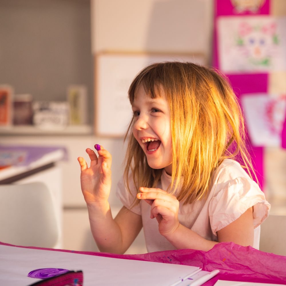 A young girl sat at a desk with paint of her hands