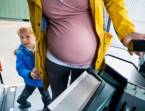 A pregnant woman in a yellow coat getting onto a bus with a young boy in school uniform