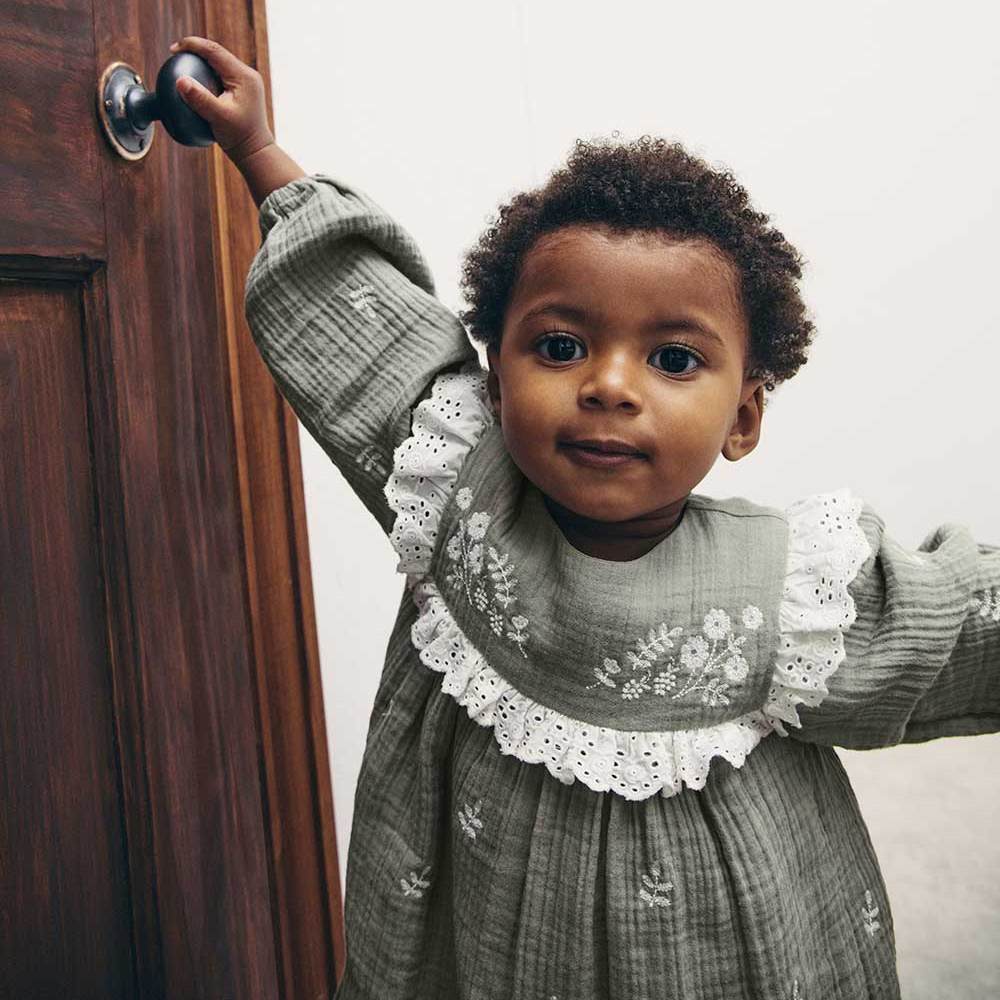 A young girl stood next to a door with her hand on the door handle