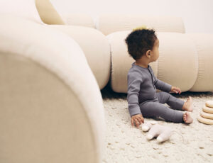 A young boy sat on the floor next to a sofa and two toys