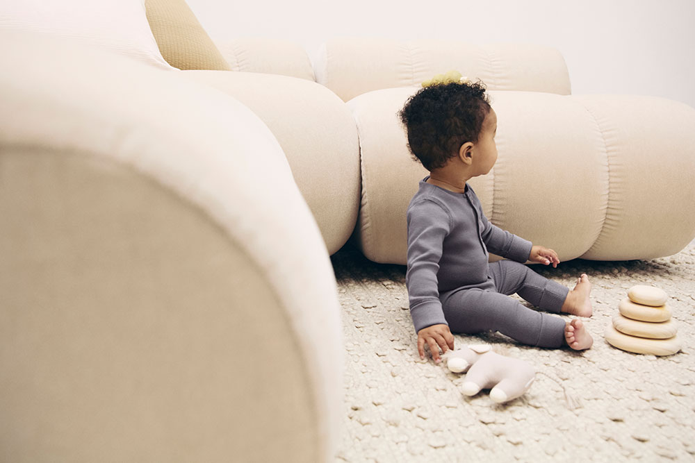 A young boy sat on the floor next to a sofa and two toys