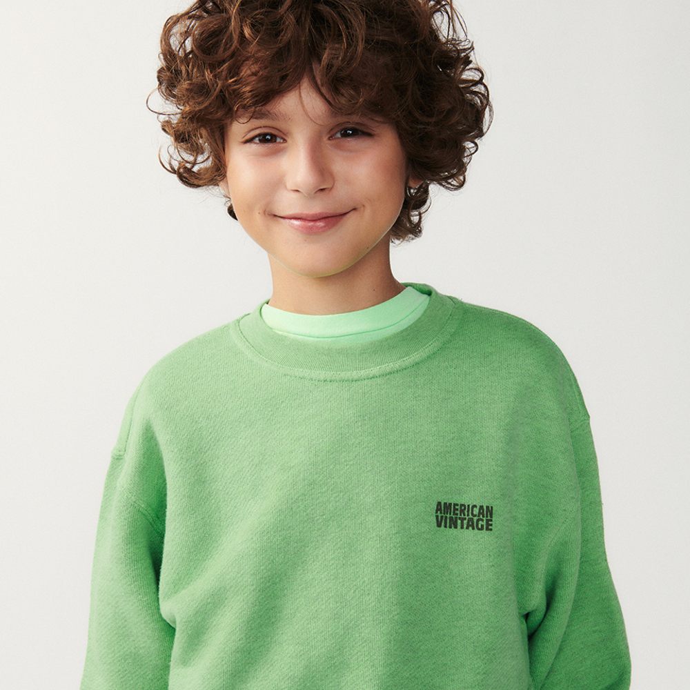 A boy smiling at the camera wearing a green sweatshirt with American Vintage written on it