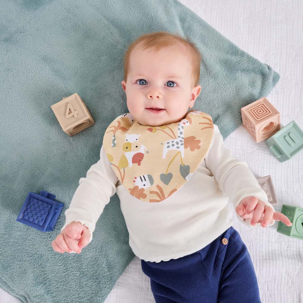 A young baby in a bib lying on a play mat beside building blocks 