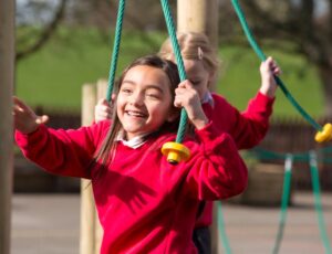 Two young girls on a climbing frame wearing red school jumpers