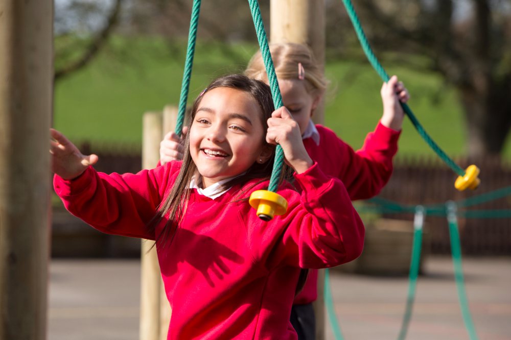 Two young girls on a climbing frame wearing red school jumpers