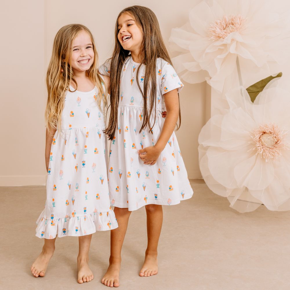 Two young girls in dresses stood side by side laughing 