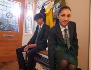 Two school children in uniform sat in the hallway of a house