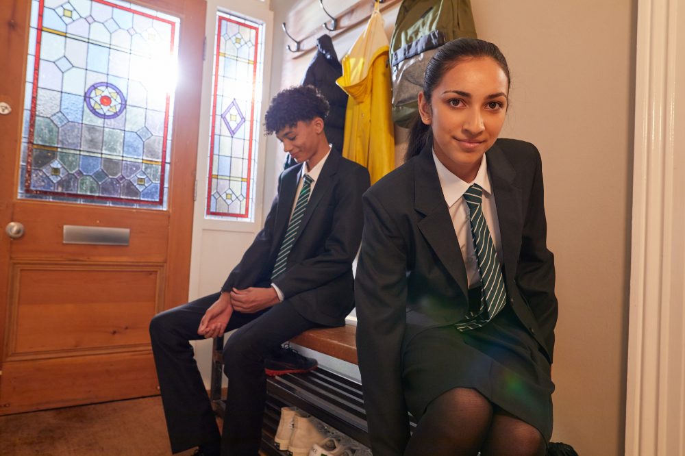 Two school children in uniform sat in the hallway of a house