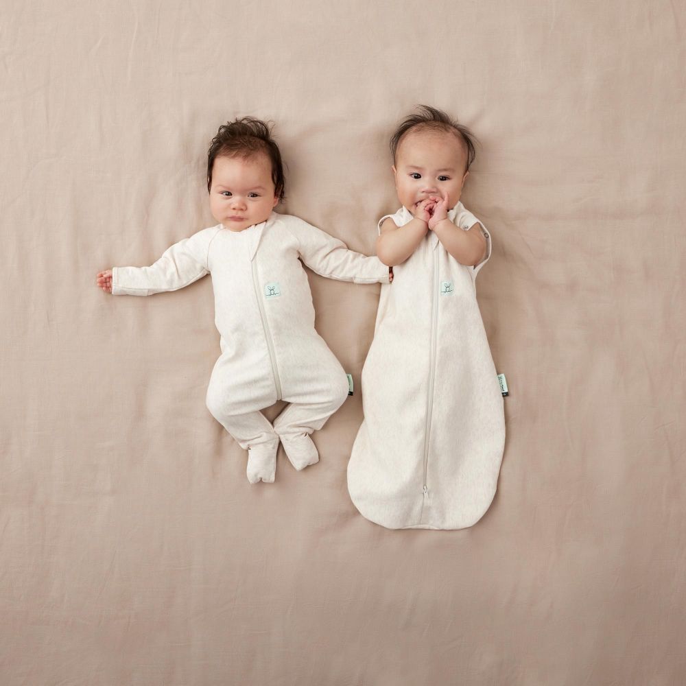 Two young babies dressed in white lying on a beige sheet