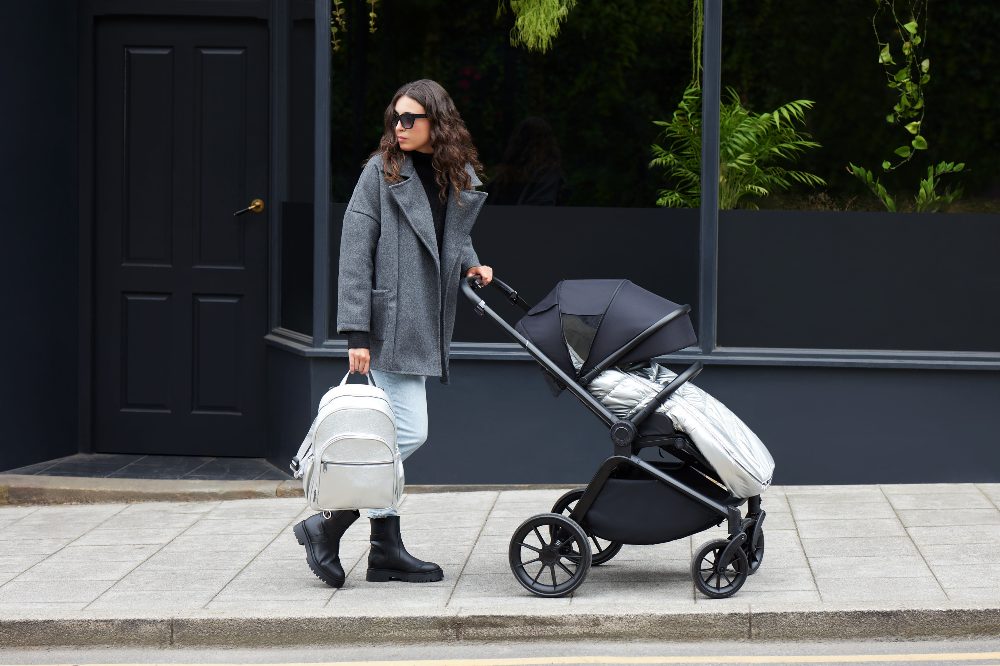 A woman outside on a street pushing a pram and carrying a baby changing bag from Ickle Bubba's Limited-Edition Chrome Collection