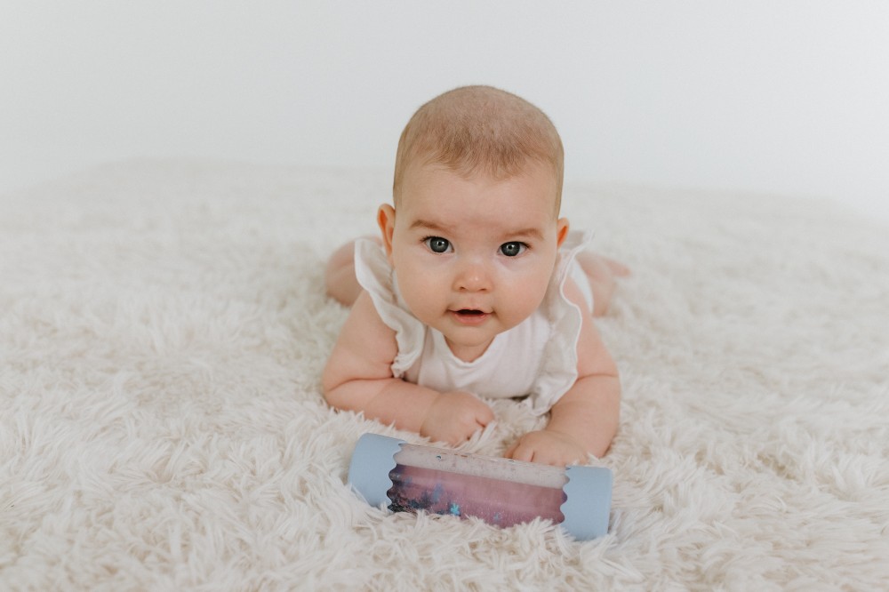 A baby lying on the floor on a fluffy rug with a toy 