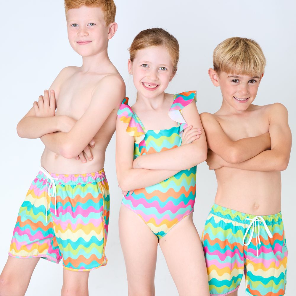 Three children stood in matching brightly patterned swimwear 