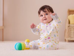 A baby sat on the floor wearing a patterned sleepsuit from the MORI x Lovevery collaboration