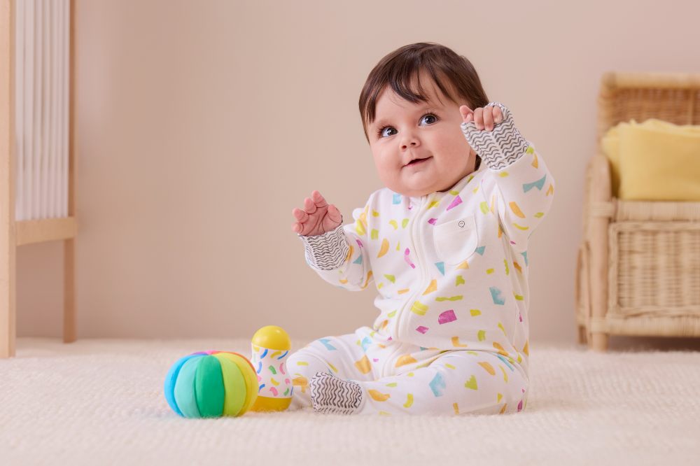 A baby sat on the floor wearing a patterned sleepsuit from the MORI x Lovevery collaboration