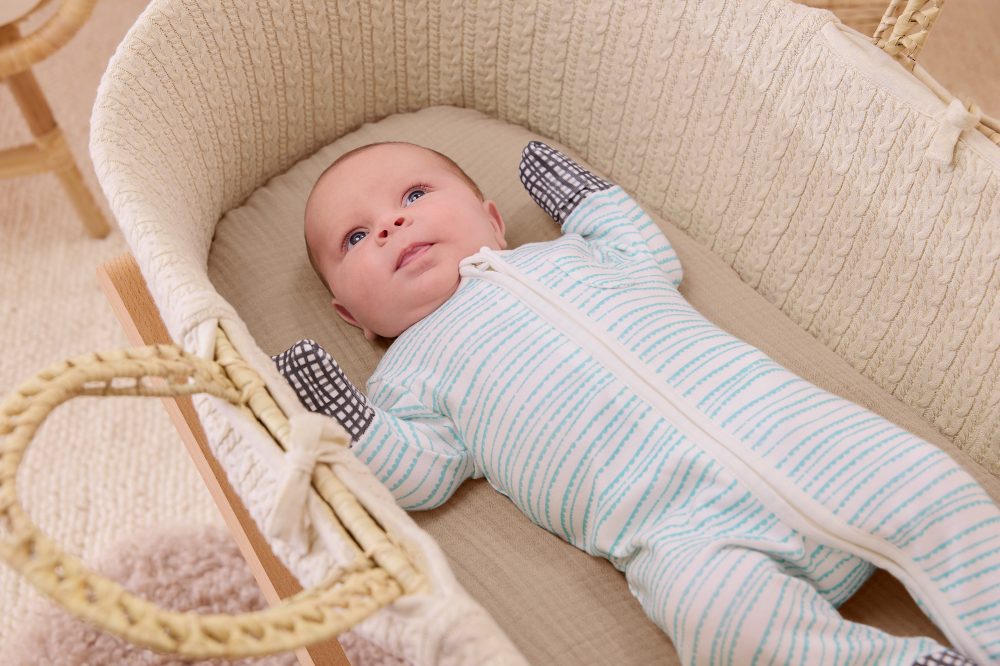 A newborn baby lying in a cot wearing a blue striped sleepsuit by MORI x Lovevery