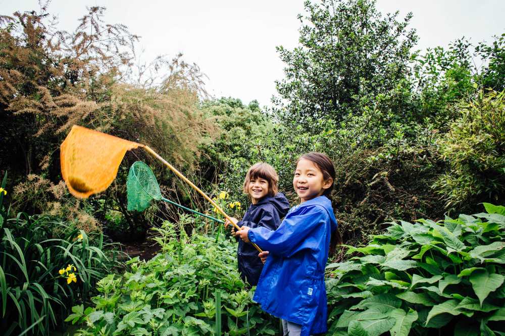 Two children outside in Muddy Puddles rainwear holding fishing nets