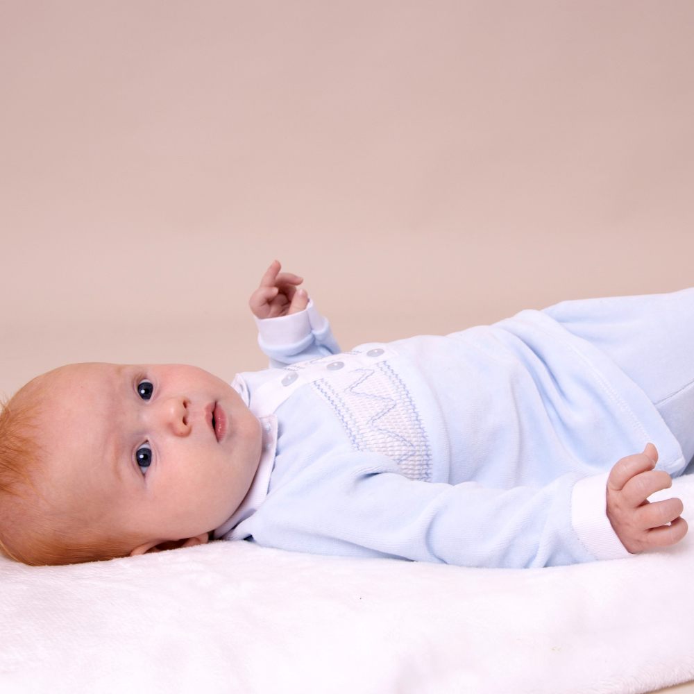 A young baby lying down in a pale blue outfit 