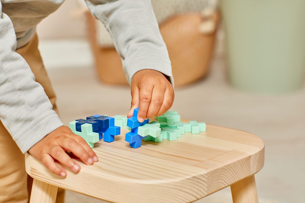 A young child playing with blue and green building pieces on a wooden stool