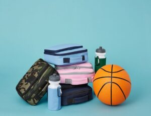 Children's lunch bags and water bottles from the Quadra School Essentials range displayed on a blue background beside a ball