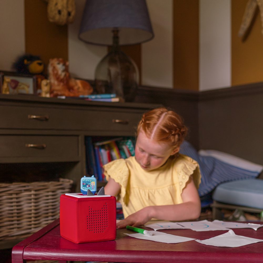 A young girl in a bedroom working at a desk with a Maths Magic Clever Pocket Tonie on it