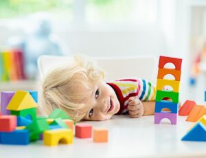 A young child with their head leant on a table full of brightly coloured building bricks