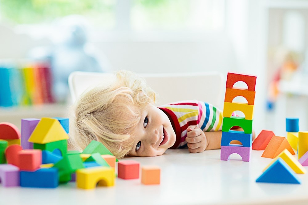 A young child with their head leant on a table full of brightly coloured building bricks