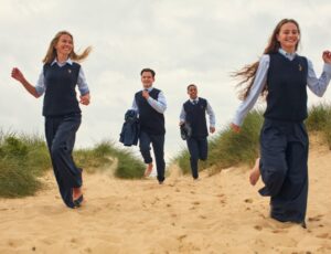 Pupils running on a beach in school uniform