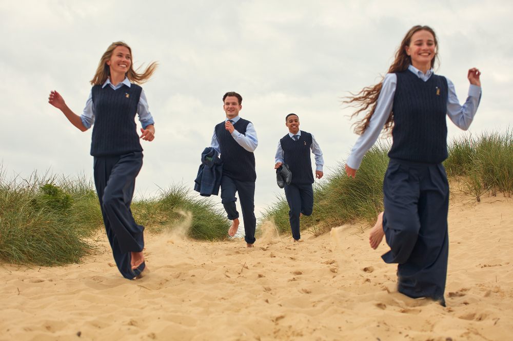 Pupils running on a beach in school uniform