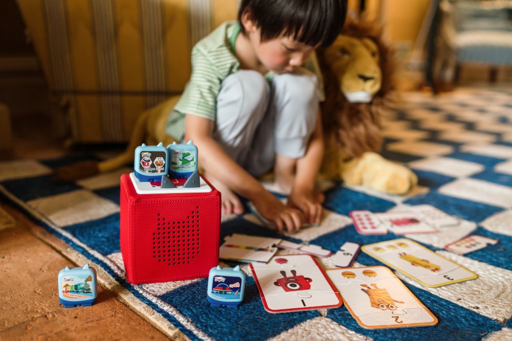 A young child sat on the floor playing with Alphablocks and Numberblocks Clever Pocket Tonie ranges