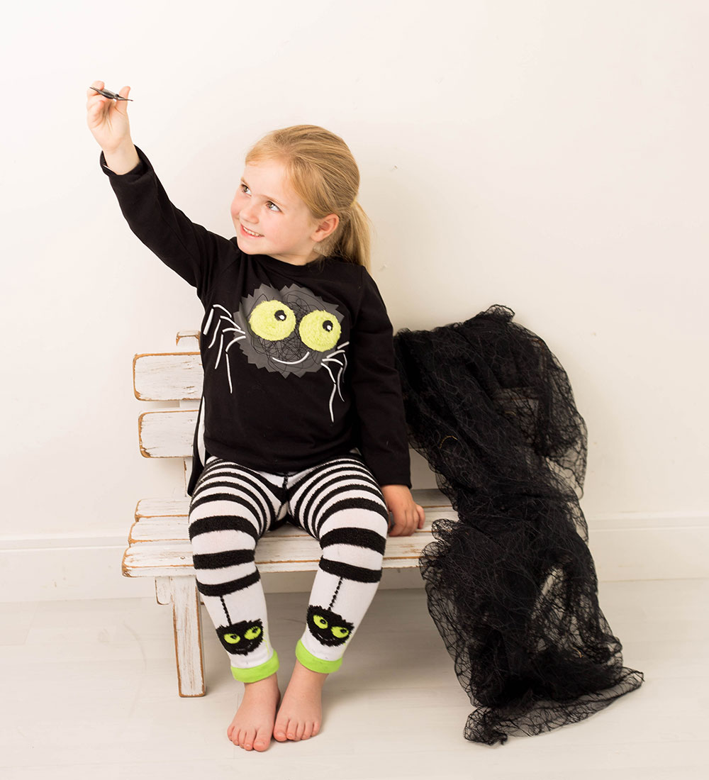 A young girl in a halloween costume sat on a bench playing with a toy