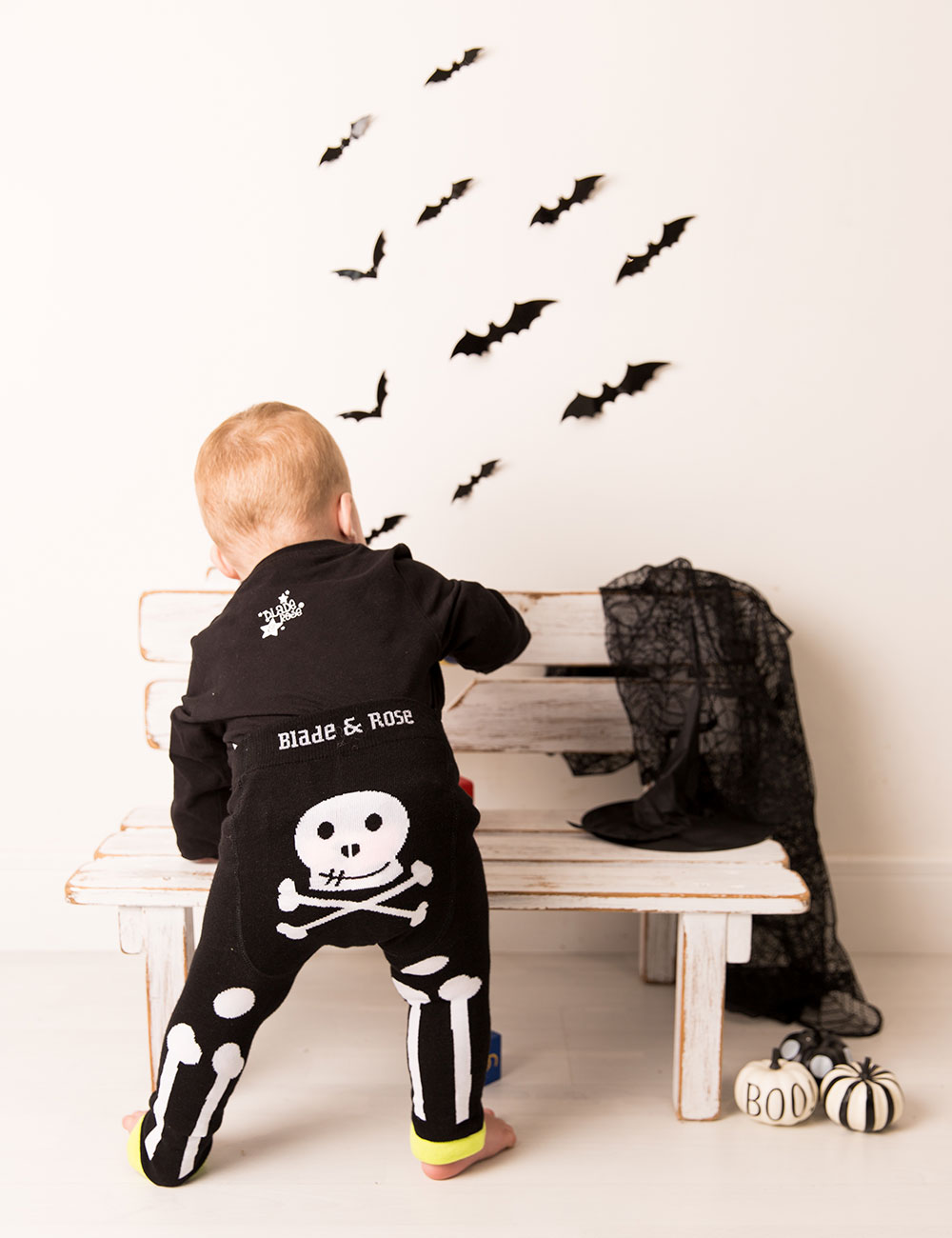 A young boy wearing a halloween costume with skull design stood playing next to a wooden bench