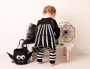 A young girl in a black and white halloween outfit stood next to a wooden bench