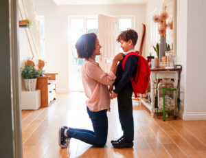 A young boy's mum knelt down in the hallway straightening his tie